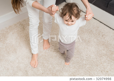 Mom teaches her daughter to walk. The child enjoys the first ste 32074998
