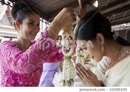 A woman in pink dress is preparing to put garland on the bride's neck A woman in pink dress is preparing to put garland on the bride's neck 32090209
