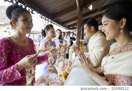 Two women are holding garland while the groom and bride are looking at it. Two women are holding garland while the groom and bride are looking at it. 32090222