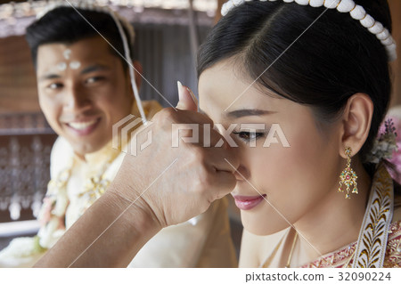 Someone uses white powder to make three dots on the bride's forehead while the groom is looking at her. 32090224
