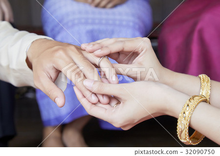 the bride is putting the ring on the ring finger of the groom 32090750