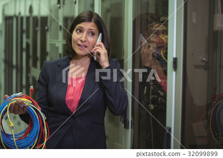 Technician holding patch cable while talking on mobile phone Technician holding patch cable while talking on mobile phone 32099899