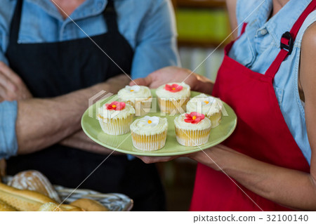 Mid section of female staff holding a plate of cupcakes 32100140