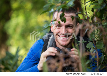 Male hiker holding binoculars in forest Male hiker holding binoculars in forest 32100328