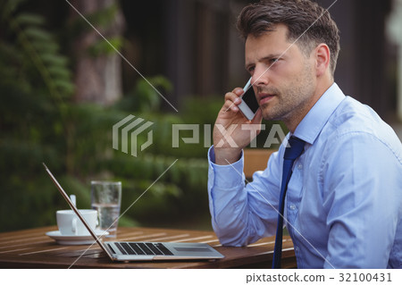 Handsome businessman talking on mobile phone while using laptop 32100431