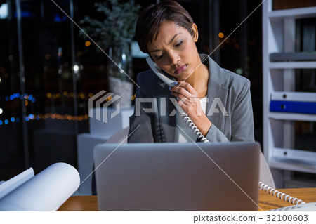 Businesswoman talking on phone while working in office Businesswoman talking on phone while working in office 32100603