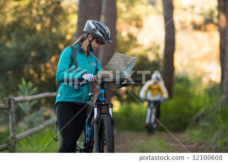 Female biker looking at a map with mountain bike Female biker looking at a map with mountain bike 32100608