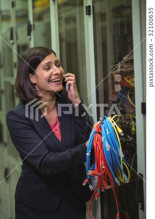 Technician holding patch cable while talking on mobile phone 32100635