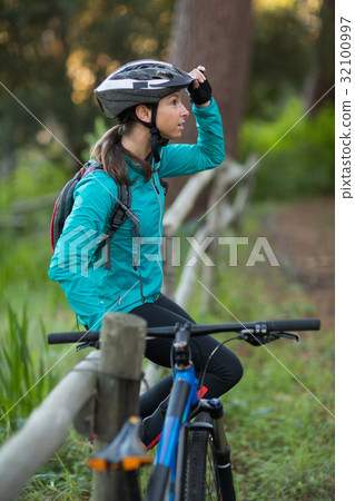 Female biker sitting on a fence in countryside Female biker sitting on a fence in countryside 32100997