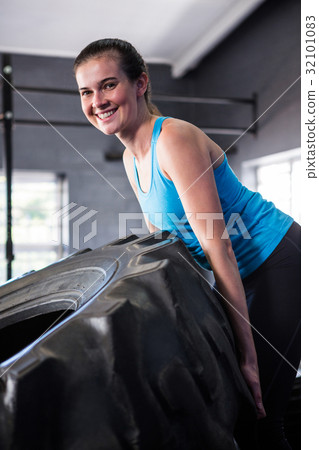 Portrait of smiling female athlete pushing tire in gym 32101083