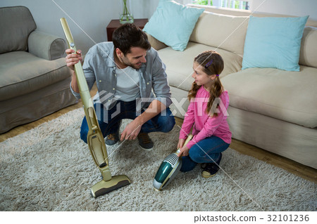 Daughter helping father to clean carpet with a vacuum cleaner