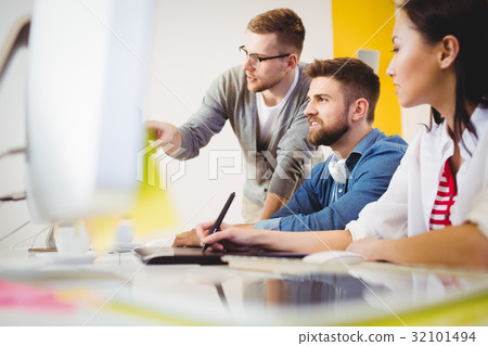 Executive pointing at computer monitor to colleagues in creative office 32101494