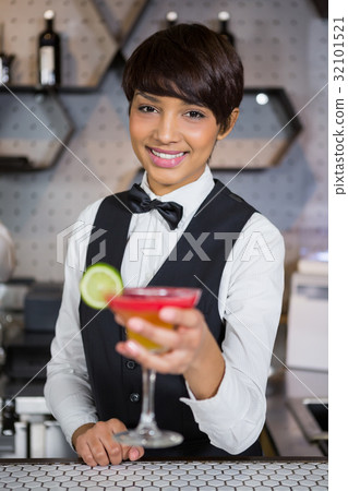 Bartender holding glass of cocktail in bar counter Bartender holding glass of cocktail in bar counter 32101521