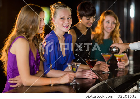 Smiling woman with cocktail standing at counter with her friends 32101532