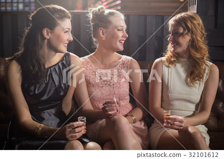 Three female friends interacting with each other while having tequila in bar 32101612
