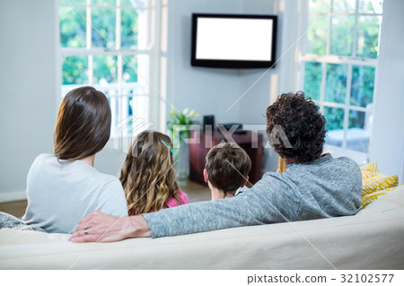 Family watching television while sitting on sofa 32102577