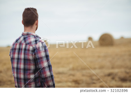 Rear view of farmer standing in field 32102896