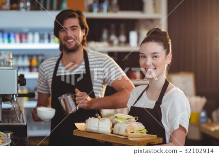 Portrait of waiter and waitress holding plate of meal and coffee jug 32102914