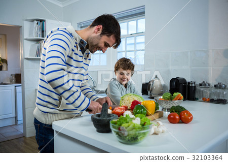 Boy looking while father chopping vegetables Boy looking while father chopping vegetables 32103364