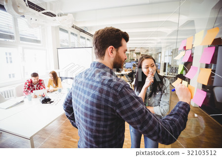Businesswoman looking coworker writing on sticky notes Businesswoman looking coworker writing on sticky notes 32103512