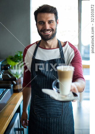 Smiling waiter holding cup of cold coffee at counter in cafe 32103872