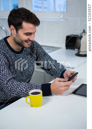 Man using mobile phone in the kitchen Man using mobile phone in the kitchen 32103937