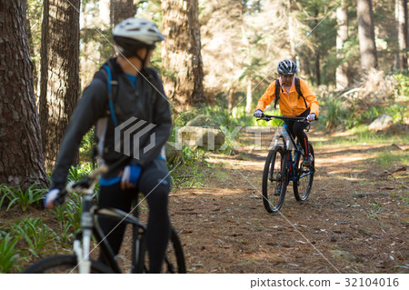 Biker couple riding mountain bike in the forest Biker couple riding mountain bike in the forest 32104016