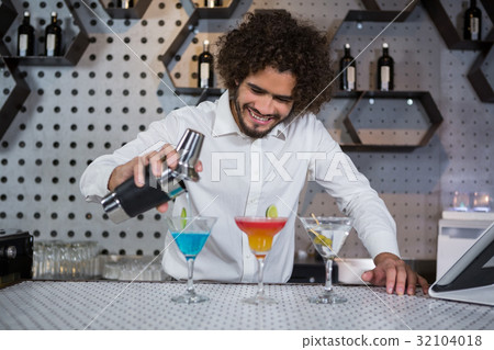 Bartender pouring cocktail into glasses Bartender pouring cocktail into glasses 32104018