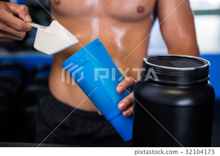 Shirtless athlete adding nutritional supplement in water 32104173