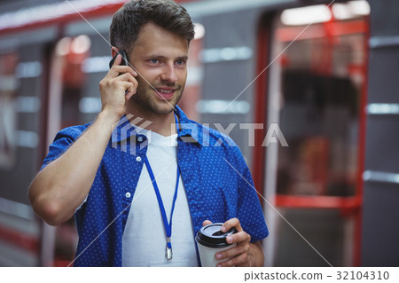 Handsome holding disposable cup while talking on mobile phone 32104310