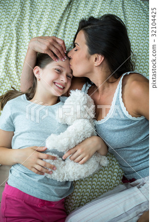 Mother kissing on daughter forehead on bed 32104425