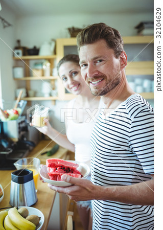 Smiling couple holding plate of water melon in kitchen Smiling couple holding plate of water melon in kitchen 32104629