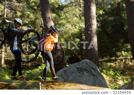 Biker couple holding their mountain bike and walking in forest 32104959