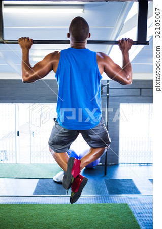 Male athlete doing chin-ups in fitness studio 32105007