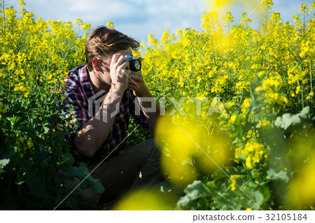 Man taking picture from camera in mustard field 32105184