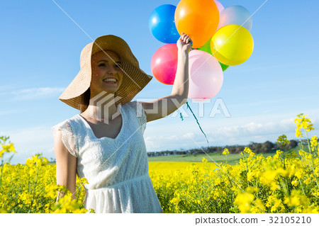 Woman holding colorful balloons in mustard field 32105210