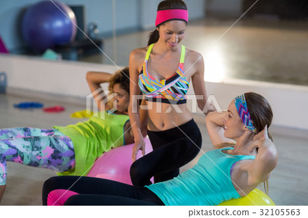 Female trainer assisting woman to exercise on exercise ball Female trainer assisting woman to exercise on exercise ball 32105563