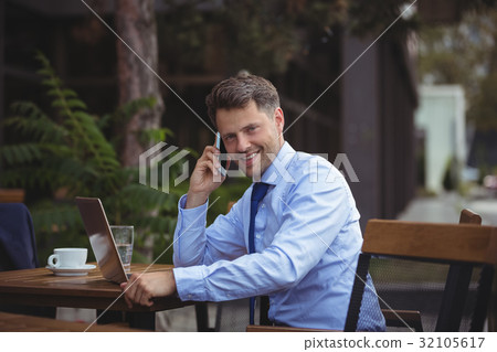 Handsome businessman talking on mobile phone while using laptop 32105617