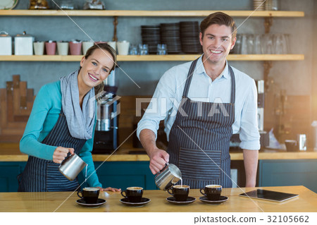 Smiling waiter and waitress making cup of coffee at counter in cafe Smiling waiter and waitress making cup of coffee at counter in cafe 32105662