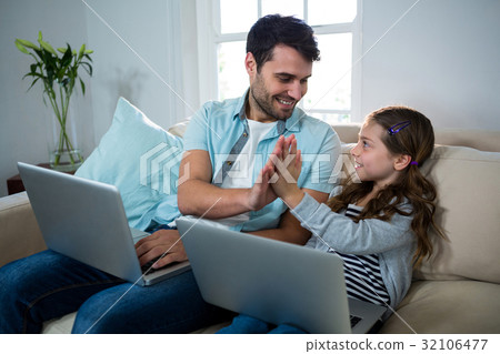 Father and daughter giving high five while using laptop in the living room 32106477