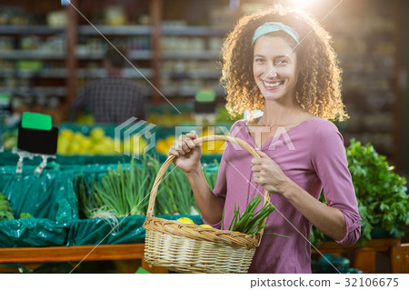 Smiling woman holding basket of vegetables in organic section 32106675