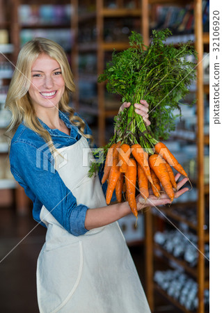 Smiling staff holding bunch of carrots in organic section 32106920