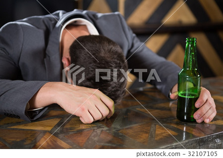 Drunk man lying on a counter with bottle of beer Drunk man lying on a counter with bottle of beer 32107105