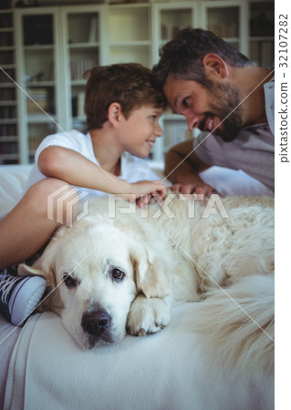 Father and son sitting on sofa with pet dog in living room 32107282