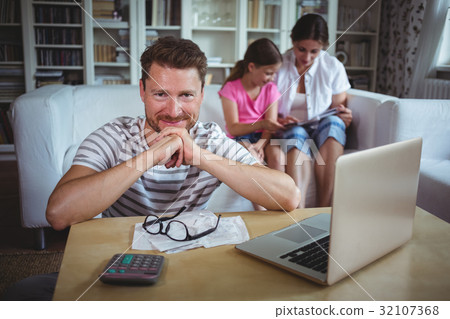 Smiling man sitting at table with bills and laptop Smiling man sitting at table with bills and laptop 32107368
