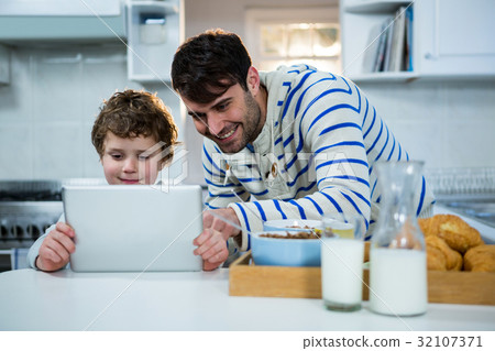 Father and son using digital tablet in the kitchen Father and son using digital tablet in the kitchen 32107371