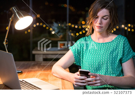 Businesswoman using mobile phone at her desk Businesswoman using mobile phone at her desk 32107373