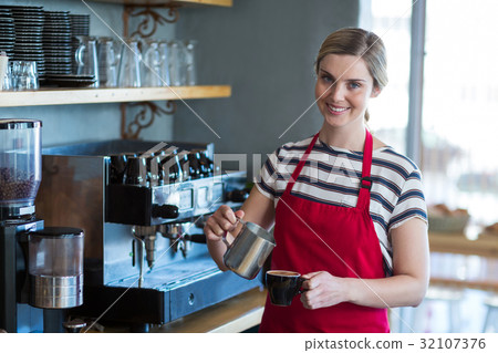 Smiling waitress making cup of coffee at counter in cafe Smiling waitress making cup of coffee at counter in cafe 32107376