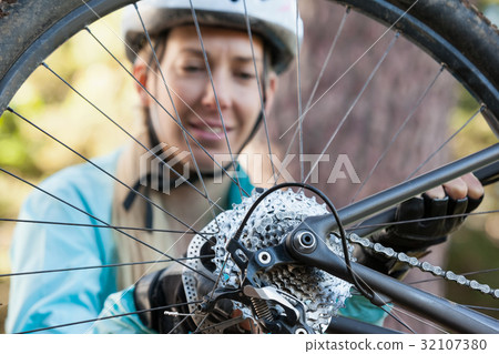 Female mountain biker examining wheel of her bicycle Female mountain biker examining wheel of her bicycle 32107380