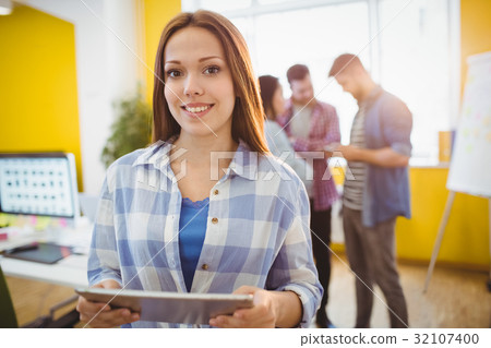 Smiling businesswoman with digital tablet standing against coworkers Smiling businesswoman with digital tablet standing against coworkers 32107400